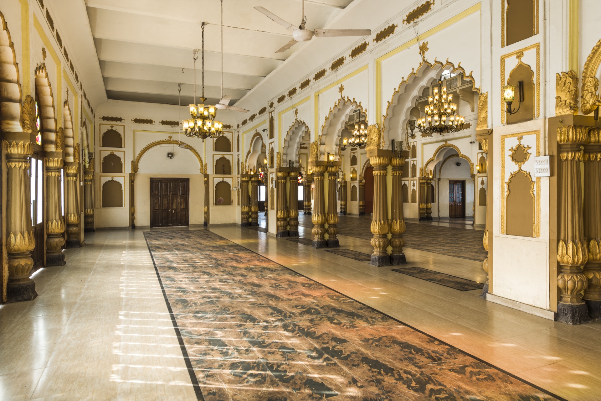 Side angle of grand hall with chandeliers and gold pillars